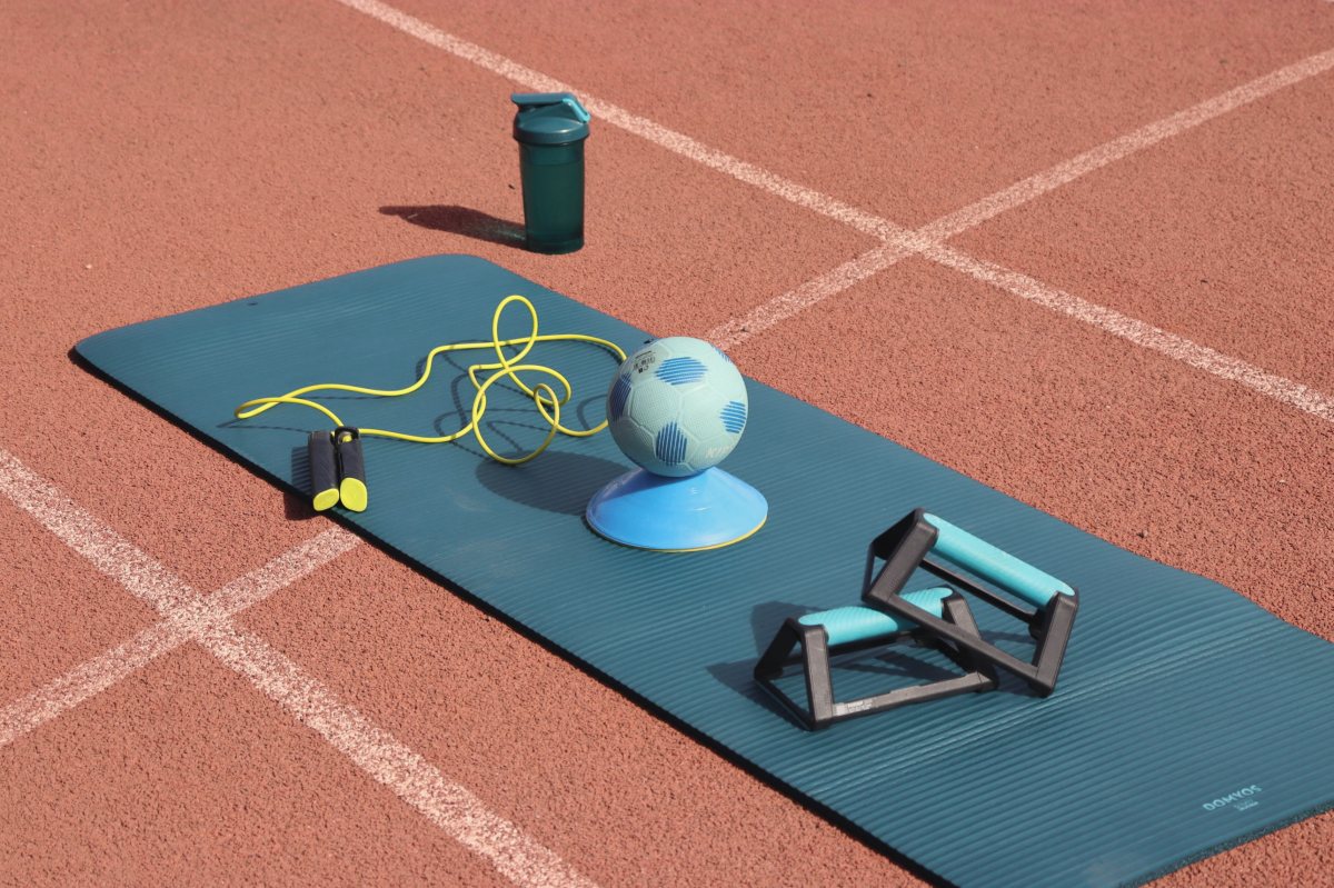 Matériel de séance posé sur un tapis, sur une piste d'athlétisme : corde à sauter, ballon, plots et pompes
